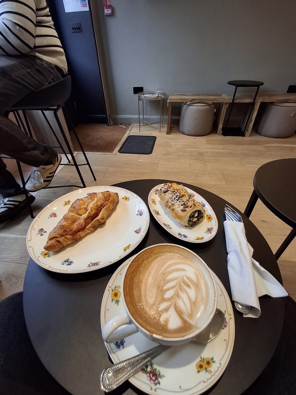 Pastries and a latte on a dark table with the cafe floor and stools behind