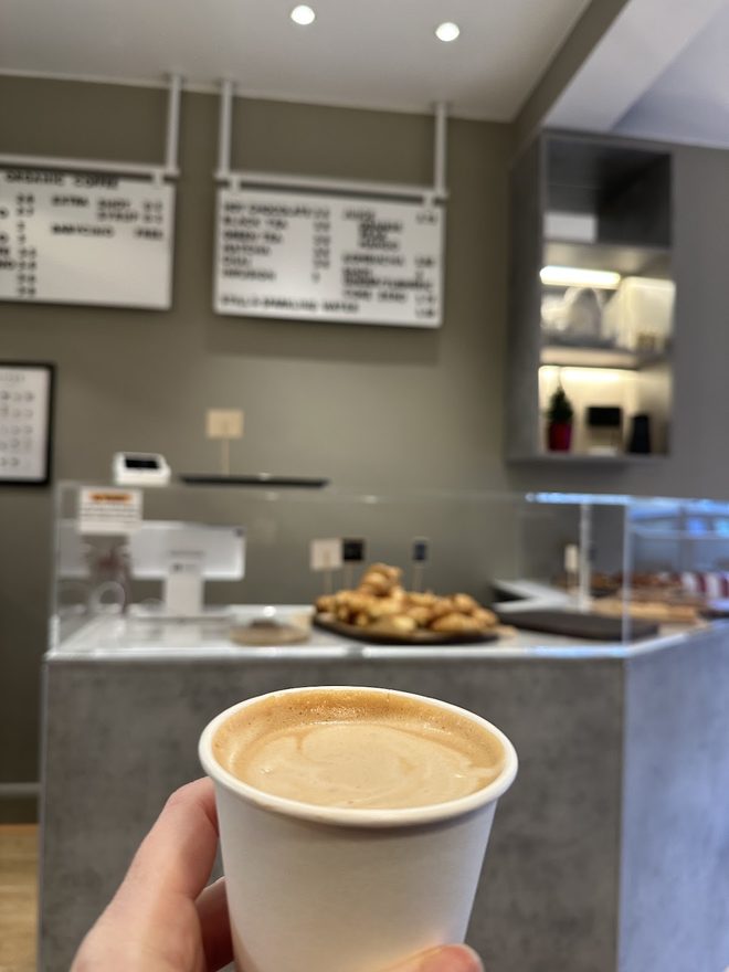 A hand holding a takeaway coffee in front of the counter