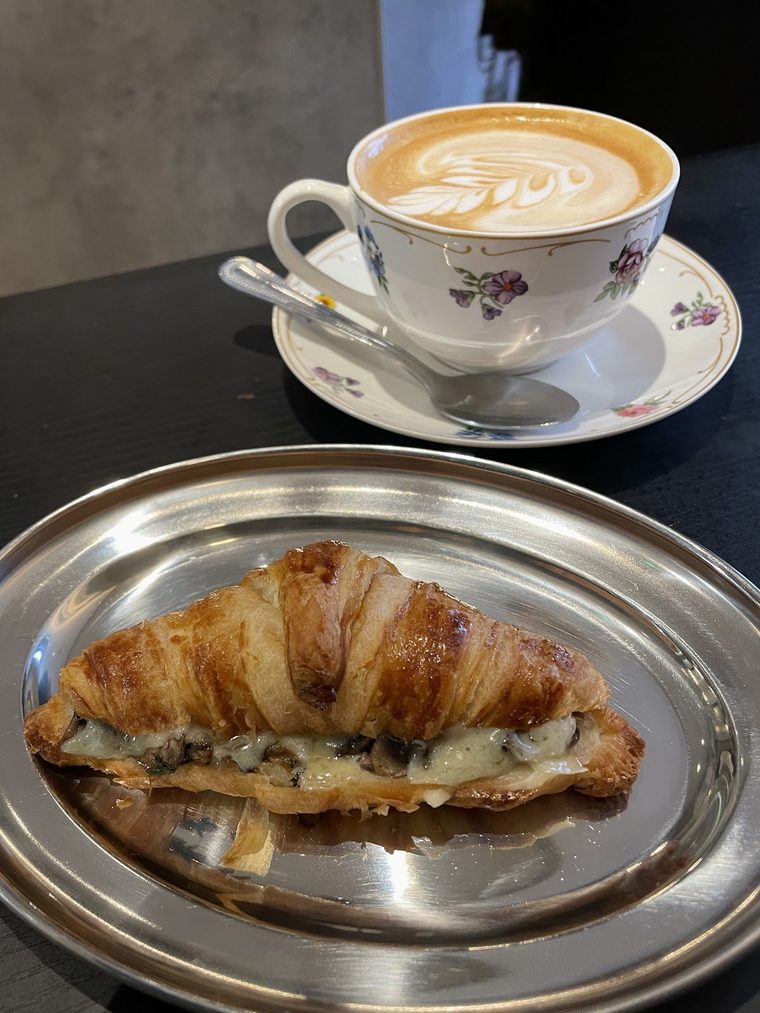 Latte with leaf art beside a toasted cheese croissant